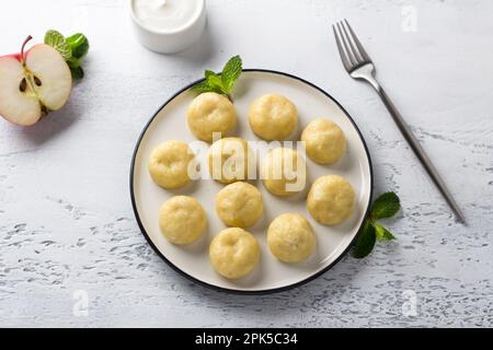 Vegetarian gluten-free steamed lazy dumplings with apple filling on a white plate, decorated with mint surrounded by half an apple and sour cream on a Stock Photo