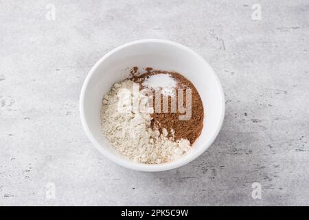 White bowl with flour, cocoa and baking powder on a gray textured background, top view. Cooking chocolate cake. Healthy homemade food concept Stock Photo