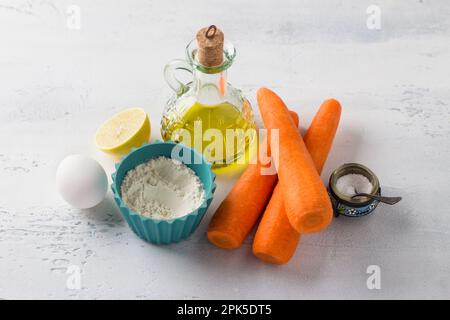 Ingredients for carrot pancakes or other vegetarian dish: carrots, flour, lemon, egg, olive oil, salt on a light gray table, selective focus. Cooking Stock Photo