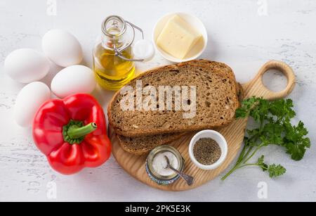 Ingredients for delicious scrambled eggs: rye sourdough bread with seeds, eggs, sweet red pepper, olive oil, hard cheese, herbs, salt and pepper on a Stock Photo