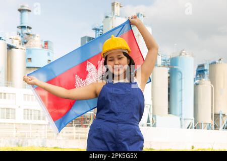 Happy asian girl in work clothes and hardhat with flag of cambodia standing in front of industrial scenery Stock Photo