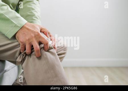 Elderly man suffering from knee pain sitting on sofa at home Stock Photo