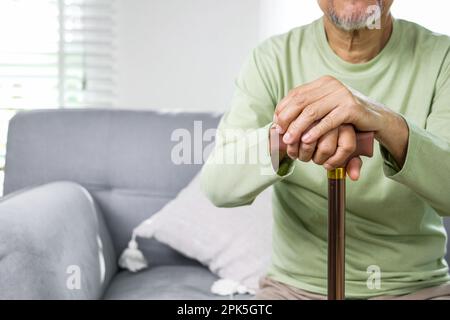 Close up hand of elderly man using walking stick trying to stand at home Stock Photo