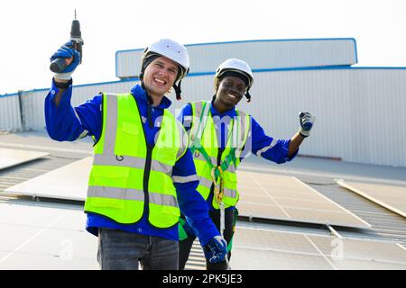 Happy engineers technicians installing solar panels on rooftop of plant Stock Photo