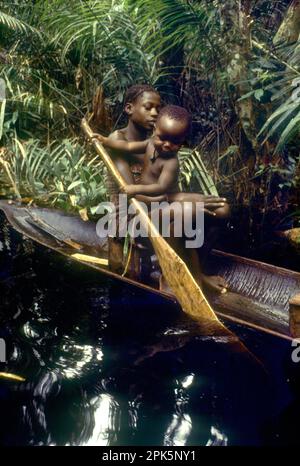 Girl of Libinza ethnic group with baby learning how to paddle in canoe in swamp forest. Ngiri river area, Democratic Republic of the Congo, central Africa. Stock Photo