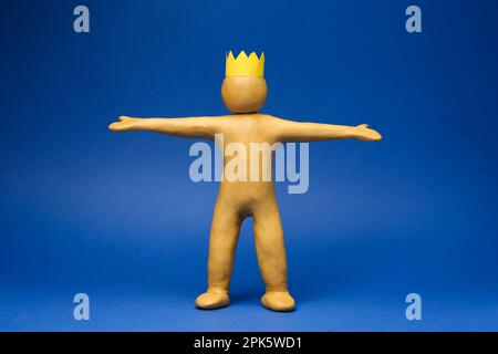 Plasticine figure with crown on head against blue background Stock Photo