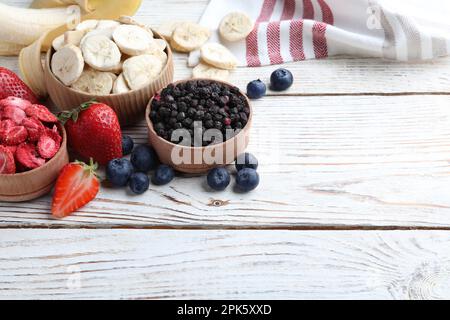 Different freeze dried and fresh fruits on white wooden table. Space for text Stock Photo