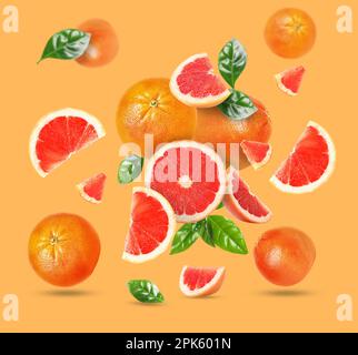 Tasty ripe grapefruits and green leaves falling on orange background Stock Photo
