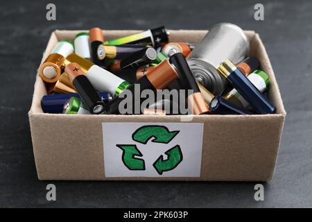 Used batteries in cardboard box with recycling symbol on black table, closeup Stock Photo