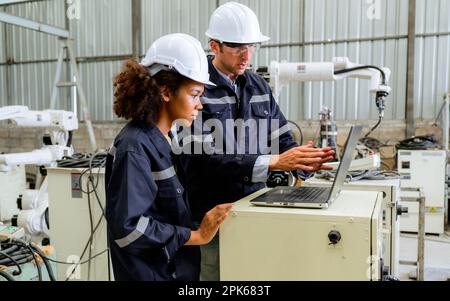 Engineers technicians controlling robotic arms on computer laptop at factory Stock Photo
