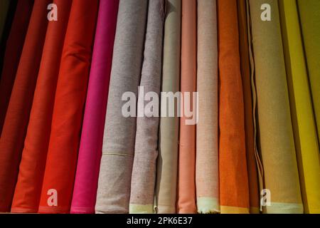 Rolls of colorful fabric on a wooden shelf in a store, solid colors, shades of red and yellow Stock Photo