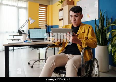 Young man with disability reading article on tablet computer when working in office Stock Photo