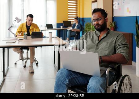 Serious software developer with disability working on laptop in open space office Stock Photo