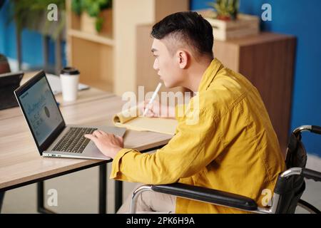 Serious businessman analyzing chart on laptop screen and taking notes in planner Stock Photo