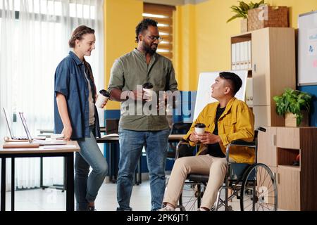 Young man with disability talking to colleagues during coffee break Stock Photo