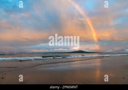 Rainbows reflected on the wet sand at Milford Beach. Rangitoto Island in the distance. Auckland. Stock Photo