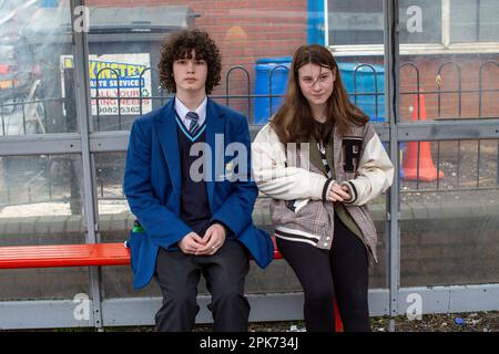 Two students waiting at a bus stop at Shankill Road in Belfast, County Antrim, Northern Ireland, UK Stock Photo