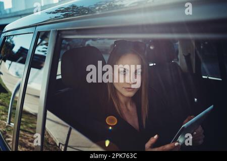 Making business plans on the move. a young businesswoman using a digital tablet while traveling in a car. Stock Photo