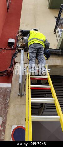 Vertical photo of an employee of the telephone or electric company on a ladder doing maintenance work on the line Stock Photo