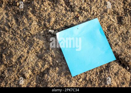 single blue square paper note laying on dried brown earth with empty free space for template or blank copy area Stock Photo