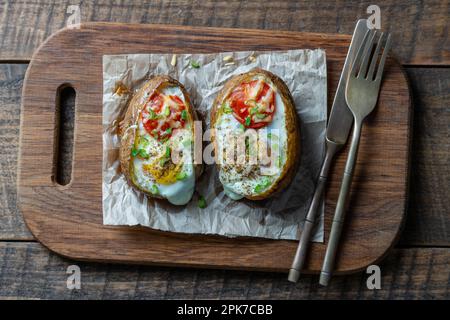 Baked potatoes stuffed with cheese, tomato, green onion and eggs on wooden background, top view, close up Stock Photo
