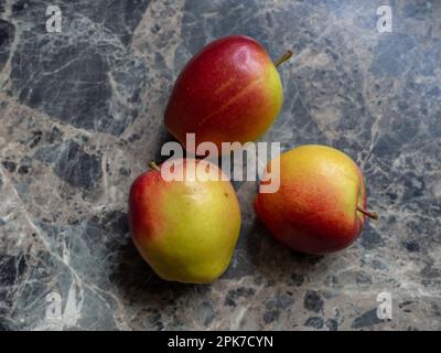 Three Braeburn apples on a black marbled kitchen worktop. Stock Photo