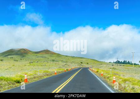 Winding road leading through the verdant green hills that surround it with protective cones lining the side of the road, reminding of the importance o Stock Photo