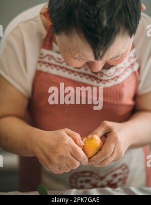 Lifestyle, education. An elderly woman with down syndrome is studying in the kitchen peel the tangerine herrself Stock Photo