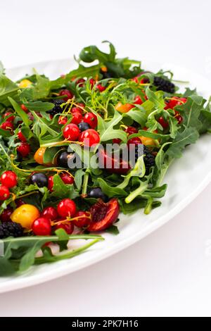 Summer delicious salad with arugula and fresh berries, red and black currants, sweet cherries and black mulberries, salad in an oval plate Stock Photo