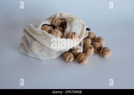 Shelled walnuts, pile of walnuts in shellin falling from a white cloth bag on a white background. Cloth bag with shelled walnuts concept photo idea. Stock Photo