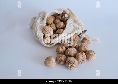 Shelled walnuts, pile of walnuts in shellin falling from a white cloth bag on a white background. Cloth bag with shelled walnuts concept photo idea. Stock Photo