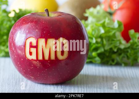 GMO text on red apple, vegetables and fruits in background, concept of genetically modified foods Stock Photo