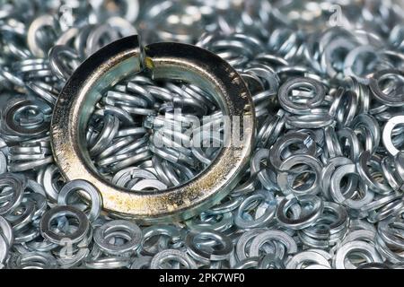 Closeup of big steel spring lock washer on texture of small stainless split washers heap. Metal ring to screw and nut tightening bent to helical shape. Stock Photo