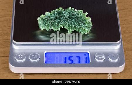 Close-up of beautiful green moldavite gemstone on weighing scale with digital display. Accurate weight determination of raw gem from meteoritic glass. Stock Photo