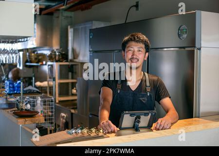 A man standing at the counter of a restaurant kitchen, using a digital tablet, the owner or manager. Stock Photo