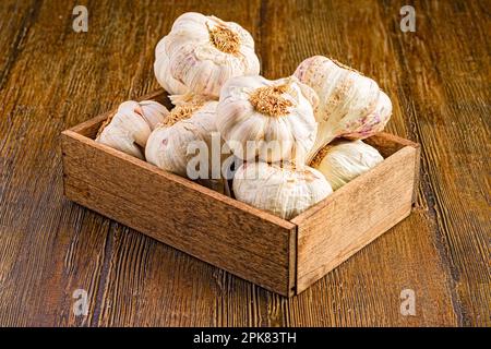 A wooden tray with several heads of garlic on a wooden surface Stock Photo