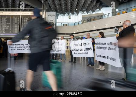 Frankfurt, Germany. 06 April 2023.  Travelers walk past protesters in front of Lufthansa counters during a demonstration at Frankfurt Airport against the airline's involvement in deportation flights to Iran. Most recently, there were two flights with deported people to Iran. Photo: Sebastian Gollnow/dpa/Alamy Live News Stock Photo