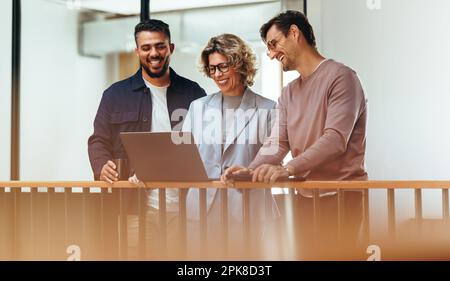 Happy business people video calling their associates on a laptop. Group of design professionals standing together and having an online meeting. Creati Stock Photo