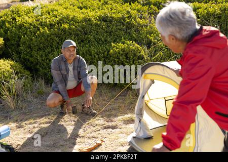 Happy senior biracial couple pitching tent in mountains Stock Photo