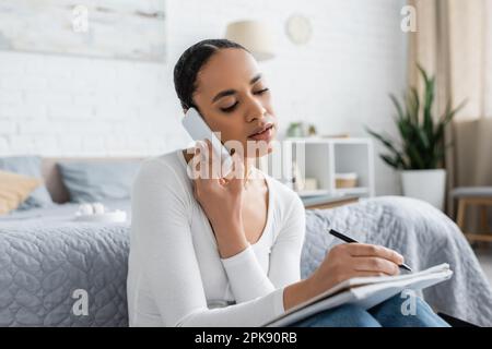 pretty african american student taking notes while talking on smartphone and studying form home,stock image Stock Photo