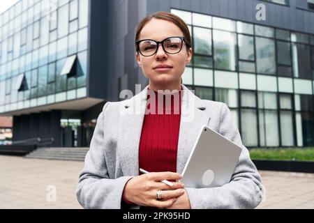 Businesswoman in glasses holding digital tablet in hands and looking at camera Stock Photo