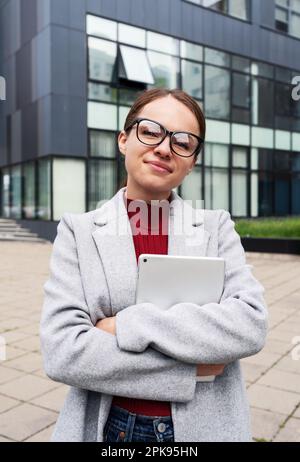 Female student wearing glasses holding digital tablet in hands and looking at camera. Stock Photo