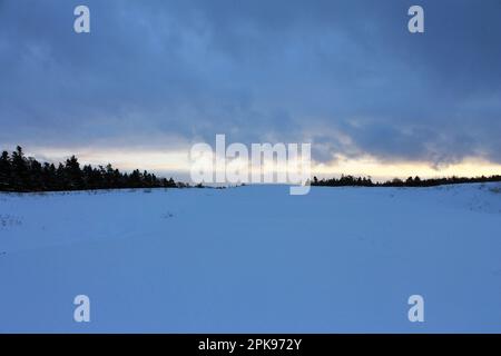 A large field covered in a layer of snow, beneath a dramatic winter sky. Stock Photo