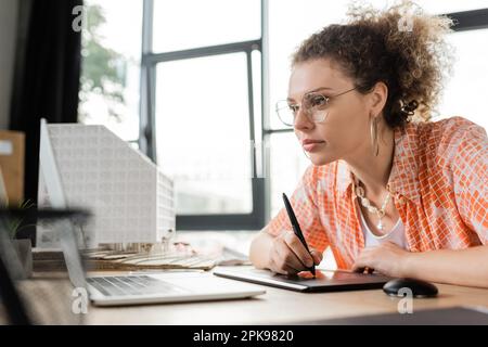 focused architectural designer using graphic tablet and looking at laptop while working in office,stock image Stock Photo