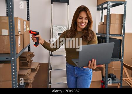Young latin woman business worker scanning package using barcode reader at office Stock Photo