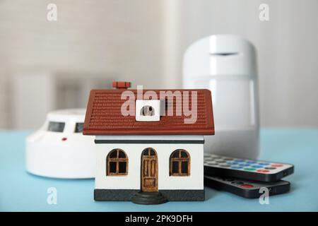 House model, remote controls, smoke and movement detectors on light blue table in room. Home security system Stock Photo
