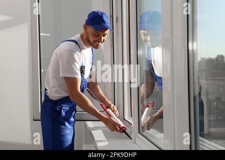 Worker sealing plastic window with caulk indoors. Installation process Stock Photo