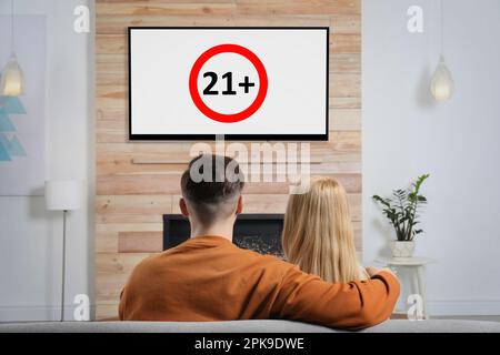 Couple watching TV with age limit sign 21+ years in living room Stock Photo