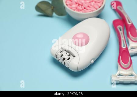 Epilator, razors and wax beads on light blue background Stock Photo