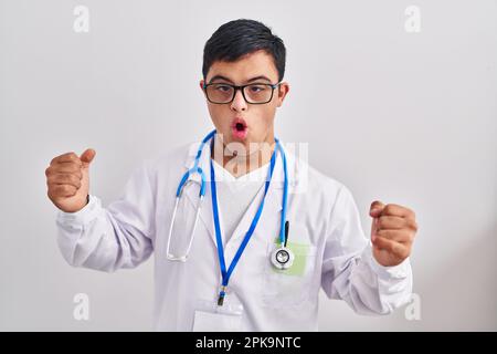 Young hispanic man with down syndrome wearing doctor uniform and stethoscope very happy and excited doing winner gesture with arms raised, smiling and Stock Photo